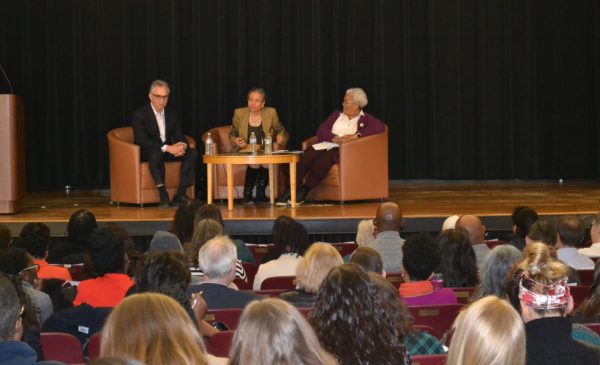 A scene from the Alumni Learning Series, with panelists sitting in chairs on the stage while audience members sit in chairs in the auditorium, listening to the discussion.