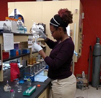 A student stands in front of a laboratory table, measuring water into a test tube.