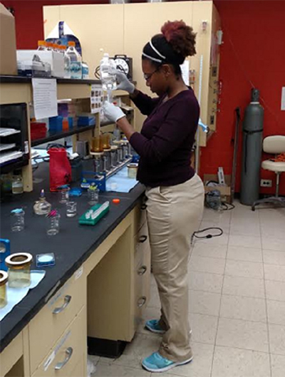 A student stands in front of a laboratory table, measuring water into a test tube.