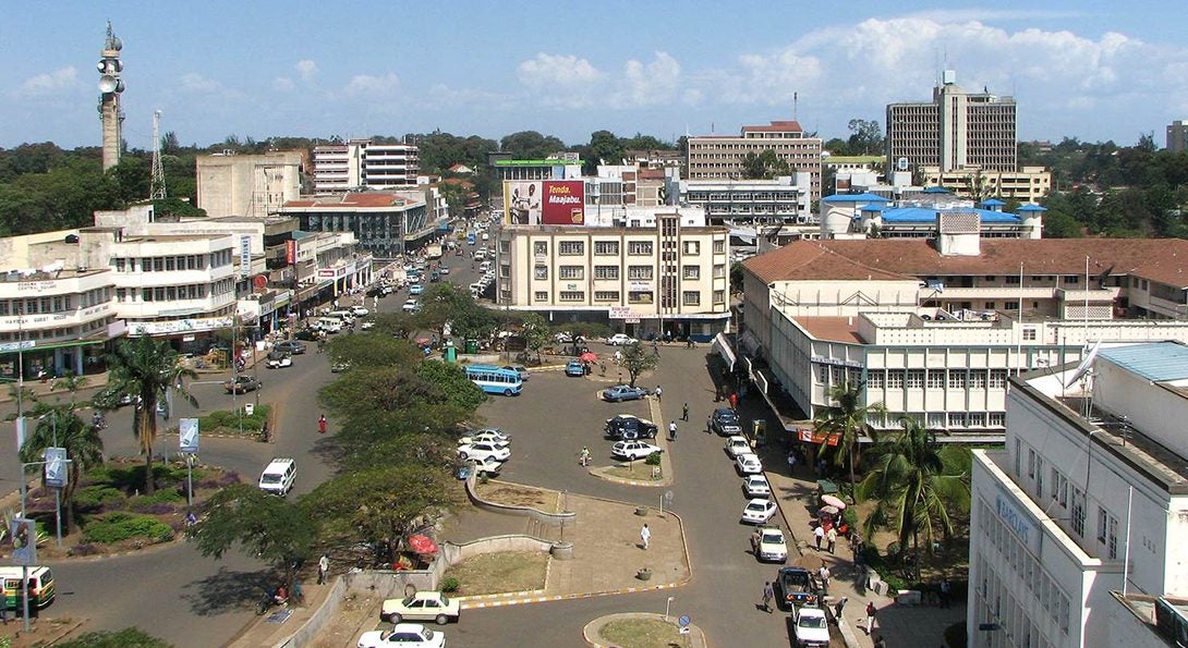 An aerial view of downtown Kisumu, Kenya, with three-story buildings lining a busy street full of cars and people.