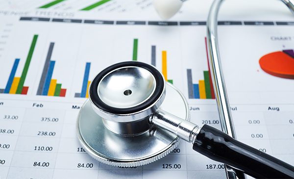 A graphical representation of health data, with a stethoscope lying on top of a piece of paper showing bar graphs and other data.