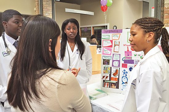 Student doctors present a poster and explain its content to a viewer.