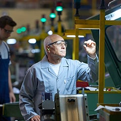 An assembly line worker examines a small metal component, holding it up to a light.