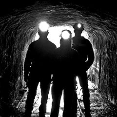 A trio of miners stand in the mouth of a mine entrance, with their headlamps lit.