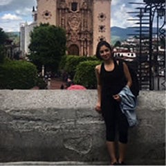 Celina Garza poses for a picture standing on a ledge, with a cathedral in Cuernavaca in the background.