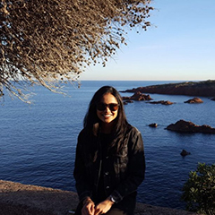 Zainab Khomusi poses for a photo standing in front of a bay with rocky islands scattered throughout it.