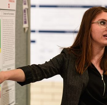 Student researcher presents her work gesturing towards a poster with data 