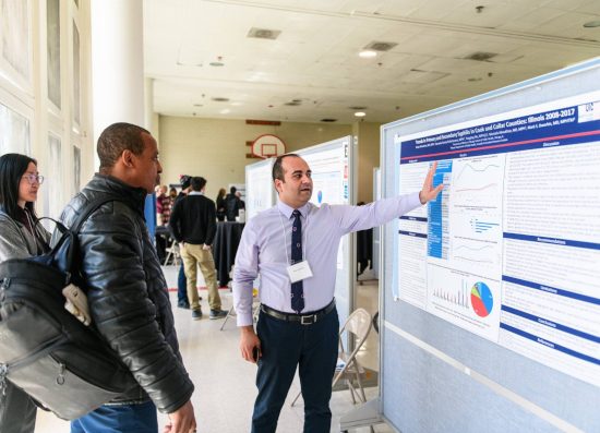 A researcher explains his poster to Research and Scholarship Day attendees.