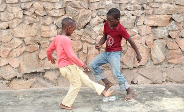 Two children are playing a game of soccer with an empty plastic water bottle.