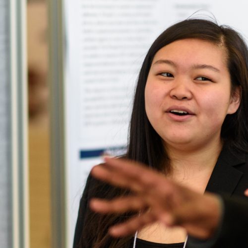 A student explains a research poster at an SPH Research and Scholarship Week presentation.