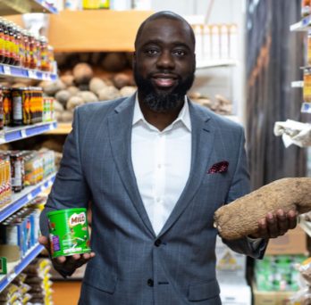 MHA alumnus Sobitan Boyede stands in a grocery aisle, holding a yuca and a canned good product.
                  