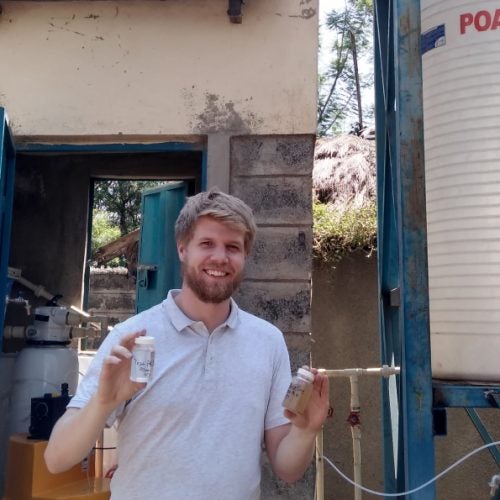 SPH student Colin Hendrickson holds up two vials of water samples at a water purification station in Kenya.