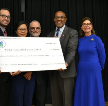 HUD Midwest Regional Administrator Joseph Galvan poses for a picture with SPH researchers and Dean Wayne Giles, holding a large cardboard check with the grant funding amount listed on it.
                  