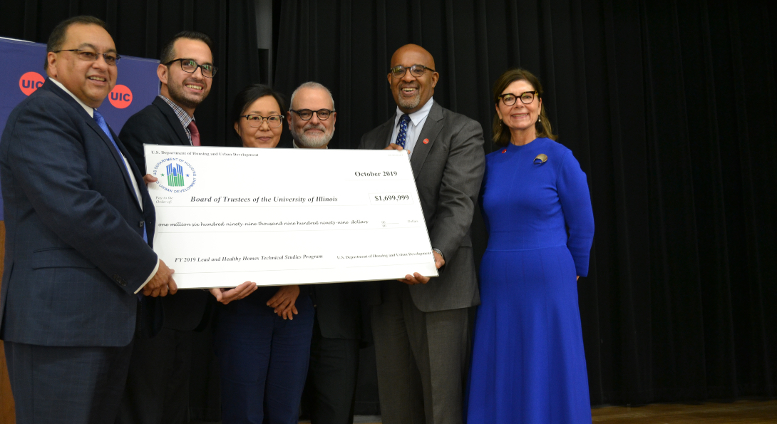 HUD Midwest Regional Administrator Joseph Galvan poses for a picture with SPH researchers and Dean Wayne Giles, holding a large cardboard check with the grant funding amount listed on it.