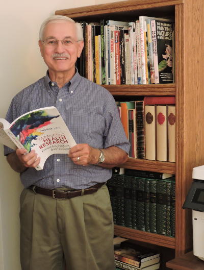 Fred Kviz stands in front of a bookshelf, with a book in hand, posing for a picture.