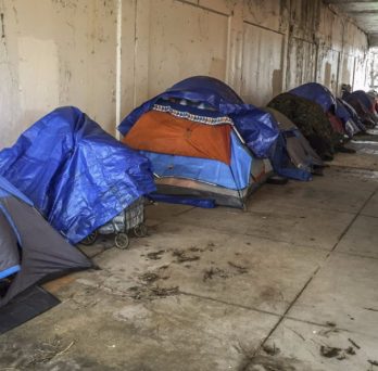 A group of tents lined up under an overpass in Chicago, presumably the temporary place of living for homeless residents of the city.
                  