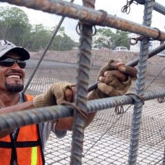 A construction worker uses a metal tool to tighten bars on a metal frame.