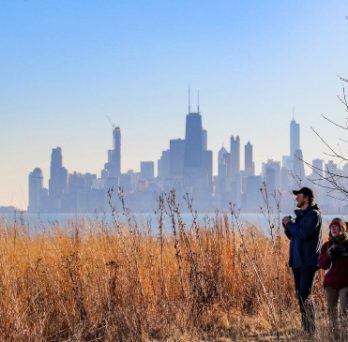 Hikers pause to observe the lakefront in parkland along Lake Michigan, with Chicago's skyline in the background. 