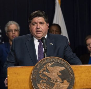 Governor Pritzker speaks from a podium at a COVID-19 press conference. 