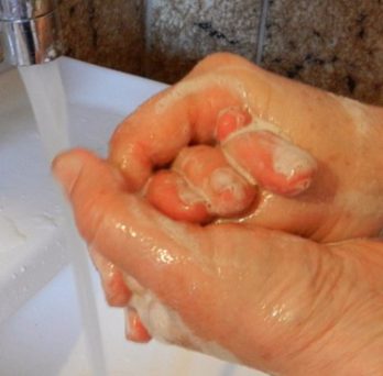 A person washes their hands with soap under a stream of water in a bathroom sink. 