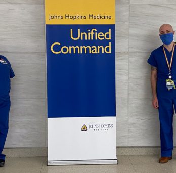 Alumni Kimberly Weems and Frankie Catalfumo pose for a photo next to a Johns Hopkins Medicine banner. 
                  