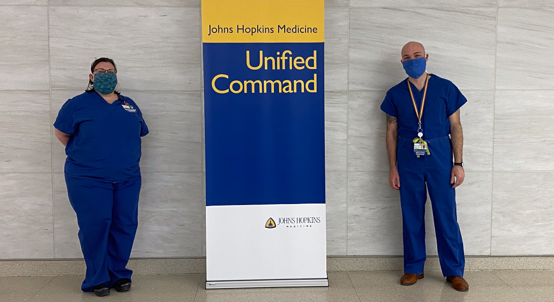 Alumni Kimberly Weems and Frankie Catalfumo pose for a photo next to a Johns Hopkins Medicine banner. 
