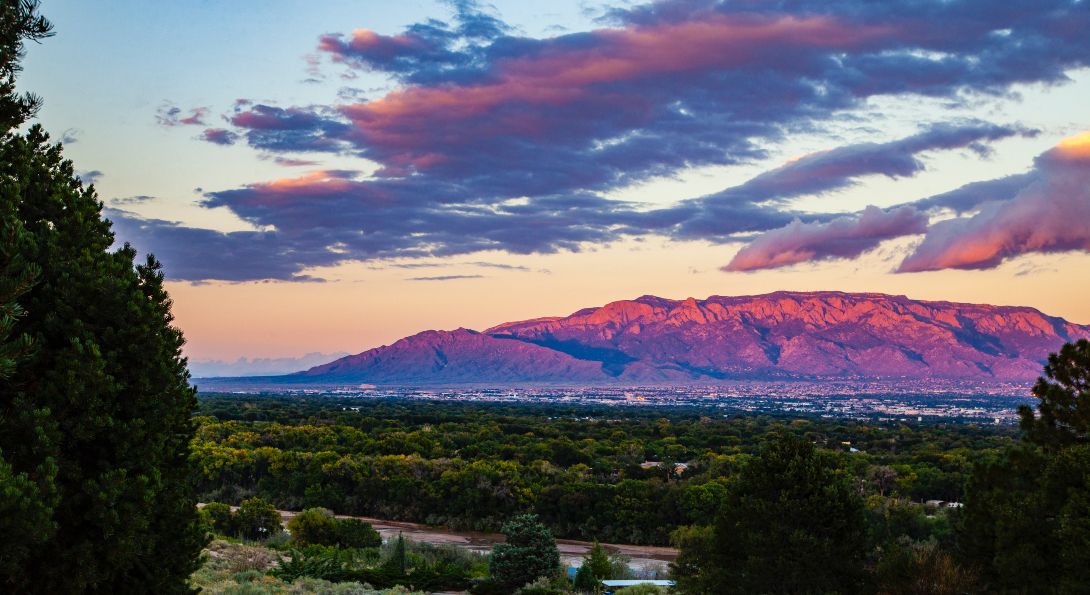 The city of Albuquerque at sunset, with mountains in the background.
