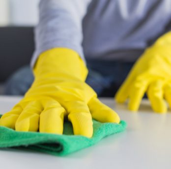 A person wipes down the surface of a table with a rag while wearing protective gloves. 