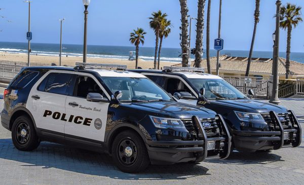 Two Huntington Beach police cars are parked near a beach, where police are monitoring beach closures during the COVID-19 pandemic.