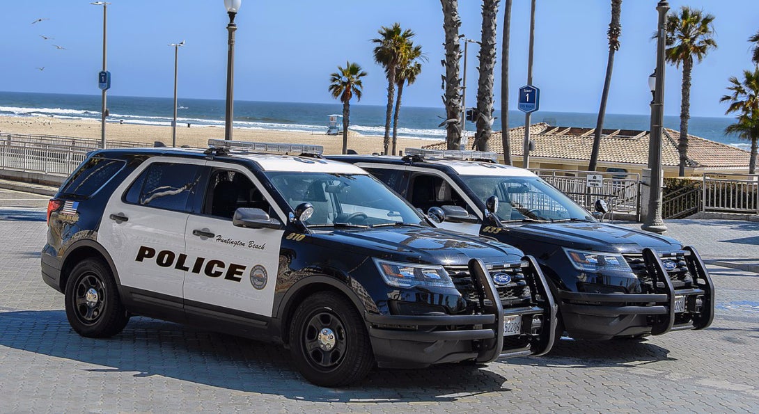 Two Huntington Beach police cars are parked near a beach, where police are monitoring beach closures during the COVID-19 pandemic.