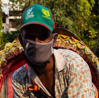A man in Bangladesh operates a rickshaw while wearing a mask. 