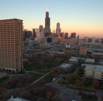 An aerial view of the Chicago skyline at dusk, with University Hall and UIC's East Campus in the foreground.
                  