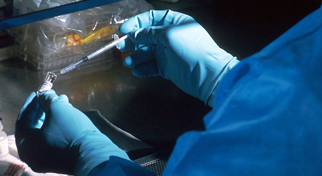 A scientist prepares a dose of a vaccine in an injection needle for a clinical trial.