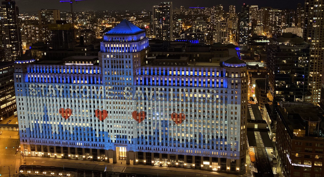 An aerial view of Merchandise Mart, lit up with a graphic of the Chicago flag and text stating 