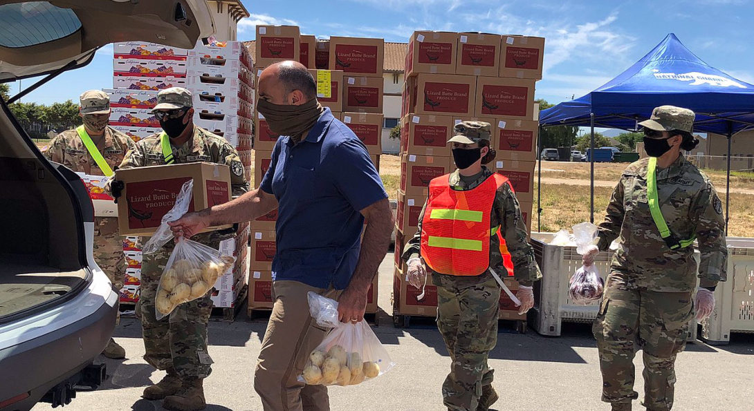 California National Guard members load potatoes into the back of a truck, with boxes of food stacked behind them.