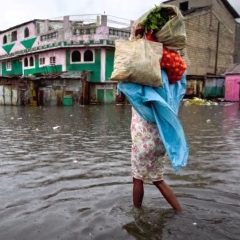 A woman wades through flood waters in a city center, with a number of possessions held in a bag on her shoulder.