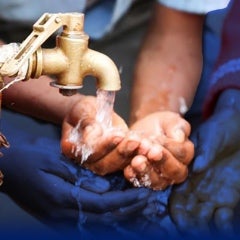 A person washes their hands from a spigot attached to a wooden post.