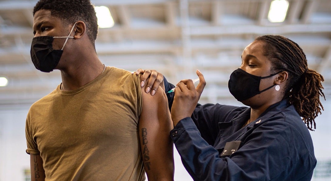 A patient receives an immunization via a shot to the shoulder area of their arm.