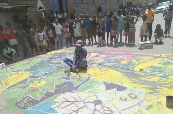 A child sits in a street atop a work of chalk art.