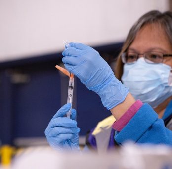 A medical professional fills a needle with the COVID-19 vaccine solution in preparation for an inoculation.
                  