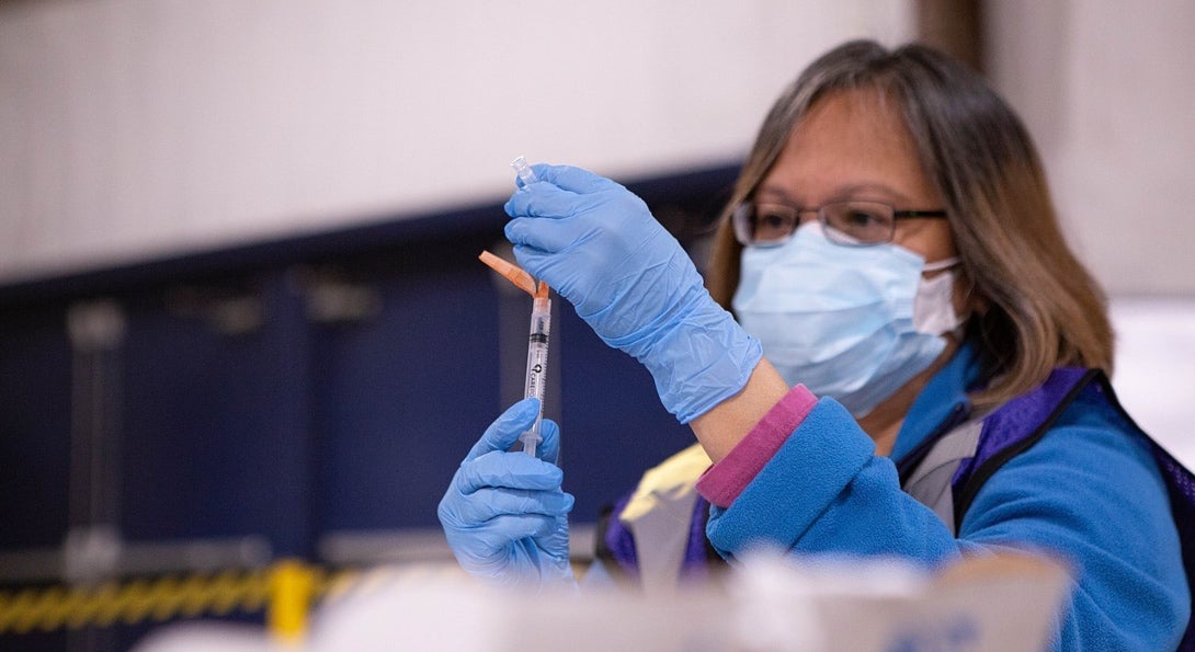 A medical professional fills a needle with the COVID-19 vaccine solution in preparation for an inoculation.