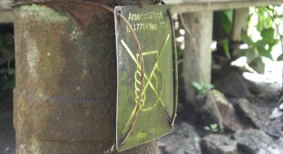 A sign is posted on a stone column warning people of high arsenic levels in nearby water.