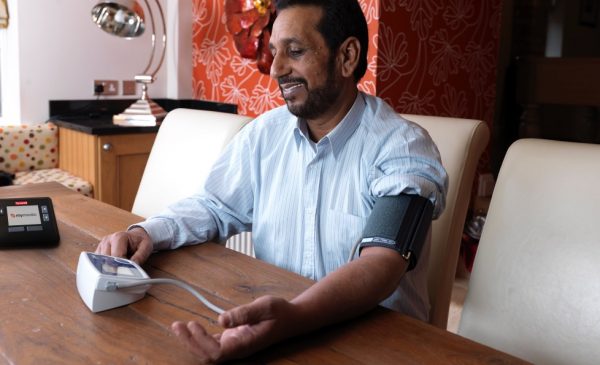 A man takes his own blood pressure using a telehealth device.