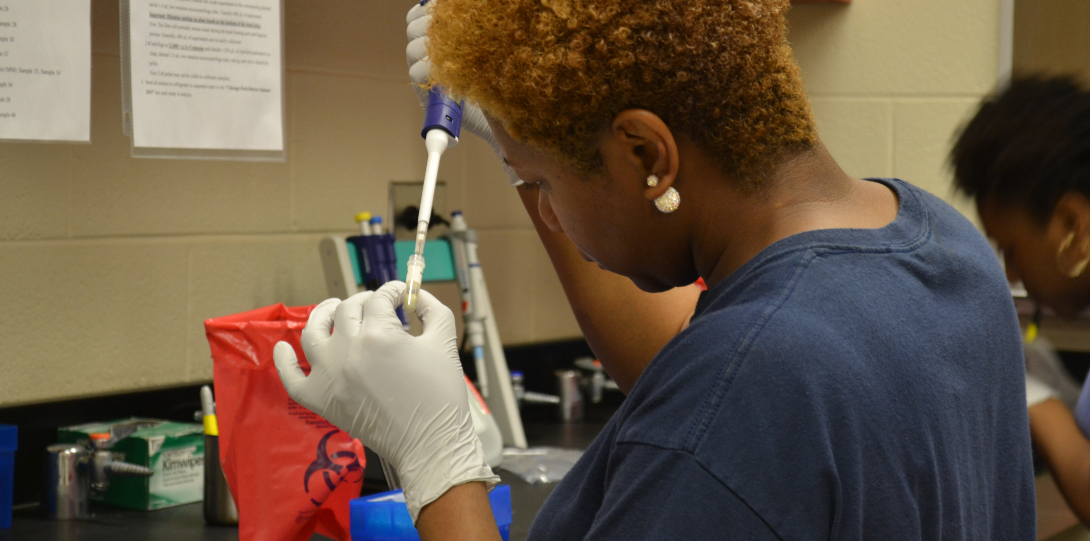 A lab technician uses a pipette to add a water sample to a small vial.