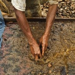 An artisanal gold miner sifts through silt in a large pan filled with water.