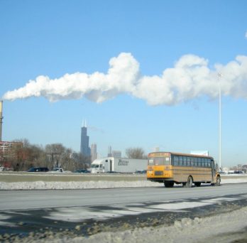 A school bus travels down Interstate 55 in Chicago, past the Crawford Generating Station, which is emitting a cloud of white smoke.
                  