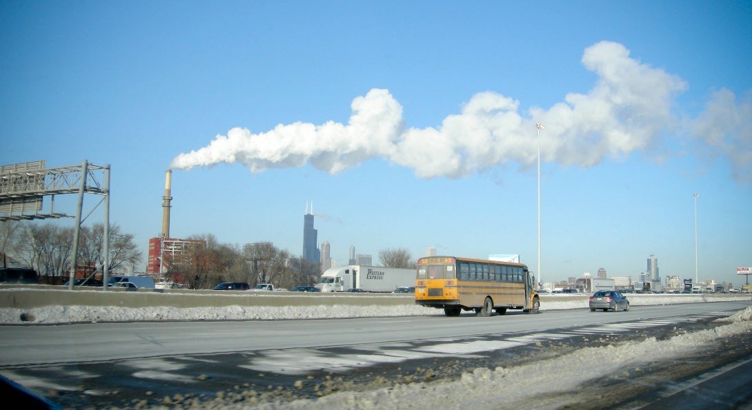 A school bus travels down Interstate 55 in Chicago, past the Crawford Generating Station, which is emitting a cloud of white smoke.