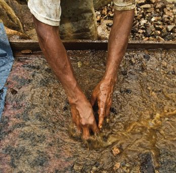 An artisanal miner sifts through silt combined with mercury in a water bath.
                  