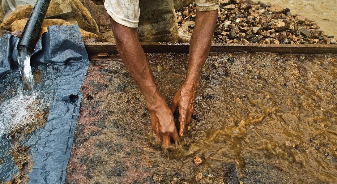 An artisanal miner sifts through silt combined with mercury in a water bath.