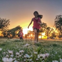 Two children run through a field of flowers.